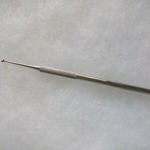 May include: A silver-colored, medical-grade probe with a textured handle and a rounded tip. The slender instrument is designed for precision and is likely used in medical or scientific applications. The probe is shown against a neutral background.