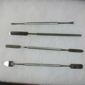 May include: Set of four stainless steel tools with different shaped tips. The tools are used for scraping, spreading, and picking up small objects.