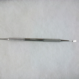 May include: A silver metal tool with a textured handle and two different shaped ends. The tool is labeled "KERR" on the handle.