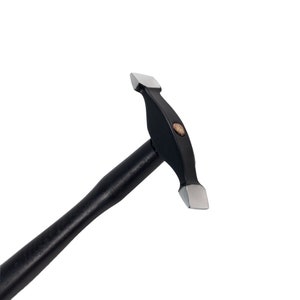 Peut inclure: Un marteau en métal noir avec un manche en bois. Le marteau a une tête plate avec un bord légèrement arrondi.