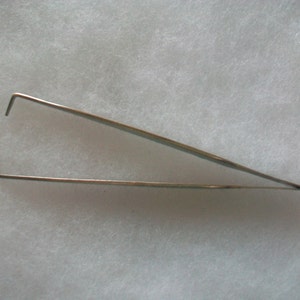 May include: A pair of silver-colored tweezers with angled tips.