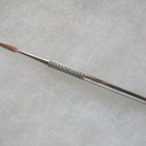 May include: A silver metal dental tool with a textured handle.