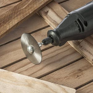 May include: A black rotary tool with a small circular saw blade attached to the end. The tool is lying on a wooden surface.