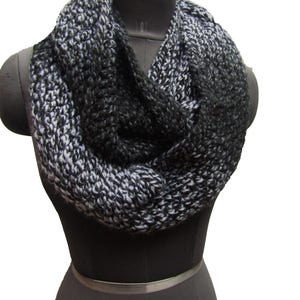 May include: A black and white infinity scarf made of a soft, textured yarn. The scarf is folded in a loop and draped over a mannequin's neck.