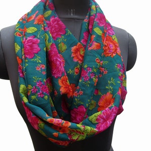 Puede incluir: Una bufanda infinita azul turquesa con estampado floral con flores rosas, naranjas y verdes.