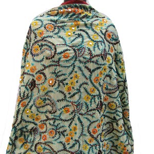 Könnte beinhalten: Ein hellfarbener Schal mit aufwendiger Stickerei. Das Design zeigt ein sich wiederholendes Muster aus Blumen- und Paisley-Motiven in Gelb, Orange und Türkis mit braunen Akzenten. Kleine, reflektierende Pailletten sind verstreut.