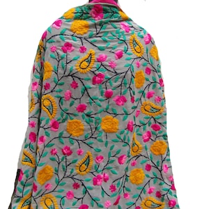 Könnte beinhalten: Ein hellgrauer Schal mit dichter Stickerei aus gelben Blumenmotiven, leuchtend rosa Blüten und dunkelgrünen Paisley-Mustern, die durch schwarze rankenartige Stiele verbunden sind. Der Stoff ist leicht und zeigt ein durchgehendes Blumenmuster.