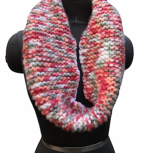 May include: A knitted cowl scarf in a multi-colored yarn with shades of pink, white, and gray.