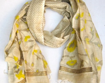May include: A cream-colored silk scarf with a yellow floral pattern and gold trim. The scarf is reversible, with a cream-colored side with small brown dots.
