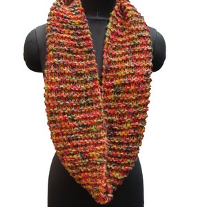May include: A hand-knitted infinity scarf in a vibrant mix of colors, including red, orange, yellow, and black. The chunky knit design creates a textured appearance. This cozy accessory is displayed on a black mannequin.