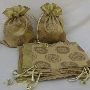 May include: A stack of gold fabric drawstring bags with a brown floral pattern. The bags are folded and tied together with a gold ribbon.