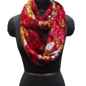 May include: A red, white, and gold infinity scarf made of soft, fuzzy fabric. The scarf is looped around a mannequin's neck.