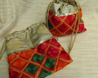 Puede incluir: Dos bolsas bordadas con cordón. Las bolsas presentan un patrón geométrico en rojo, naranja y verde, con detalles dorados. La parte superior de las bolsas es de tela de brocado dorado. El cordón es de color dorado.