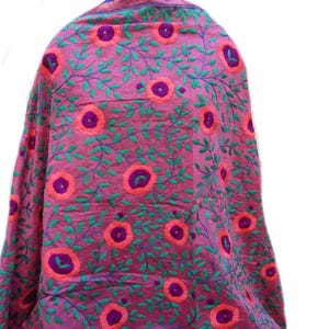 May include: A pink textile with embroidered floral and leaf patterns. The design features large, circular flowers in shades of orange and purple, surrounded by green leaves and stems. The fabric is draped, showcasing the intricate embroidery.