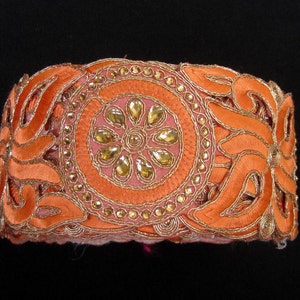 Op de afbeelding: Oranje stoffen bies met gouden borduurwerk en strass. De bies heeft een bloemmotief met een centraal cirkelmotief.