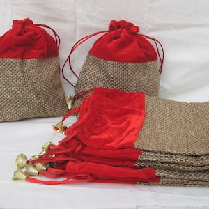 May include: A stack of red velvet drawstring bags with brown burlap bottoms. The bags are tied with gold cords and have gold tassels.