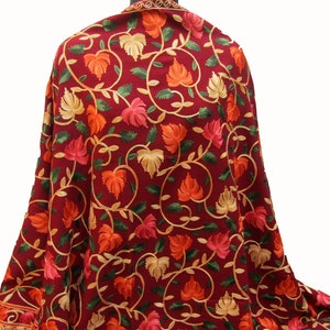 Puede incluir: Chal burdeos con un intrincado diseño de bordado floral. El chal presenta un patrón repetido de hojas en tonos naranja, rosa y dorado, con hojas verdes y vides doradas. Los bordes también están decorados con bordados dorados.