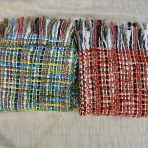 Pode incluir: Duas echarpes tecidas com bordas franjadas. Uma é principalmente azul, amarela e verde, a outra vermelha, preta e branca. As echarpes têm um padrão texturizado, semelhante a xadrez, e são exibidas em um fundo neutro.