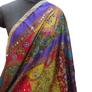 May include: A colourful silk scarf with a patchwork design featuring floral and geometric patterns. The scarf is adorned with mirror embellishments and has a gold trim.