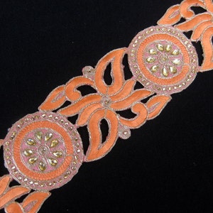 Op de afbeelding: Oranje en gouden geborduurde trim met een bloemenmotief en parelmoeraccenten. De trim is perfect om een ​​toets van elegantie toe te voegen aan elk project.