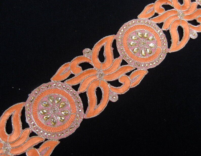 Op de afbeelding: Oranje en gouden geborduurde trim met een bloemenmotief en parelmoeraccenten. De trim is perfect om een ​​toets van elegantie toe te voegen aan elk project.