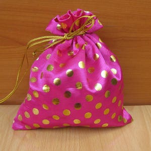 May include: A pink satin drawstring bag with gold polka dots. The bag is closed and has a gold drawstring.