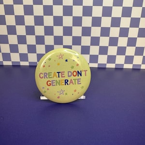 May include: A round, light yellow pin-back button featuring the text "CREATE DON'T GENERATE" in multicolored letters. The design is decorated with small, colorful star shapes scattered around the text, which is centered on the button face.