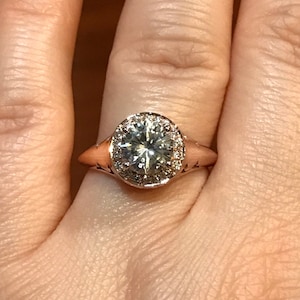 May include: A rose gold engagement ring with a large oval-shaped diamond surrounded by a halo of smaller diamonds.