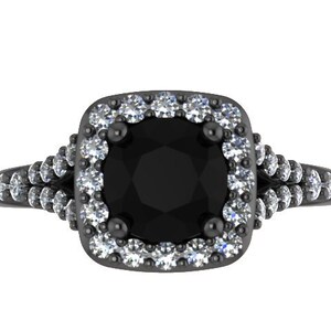 May include: A black engagement ring with a large, round, black center stone. The center stone is surrounded by a halo of smaller, white gemstones. The band features additional white gemstones. The ring has a dark, metallic finish.