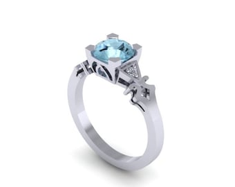 May include: A silver ring with a light blue gemstone and smaller clear gemstones. The ring has a detailed design with intricate carvings.