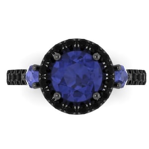 May include: A black gold engagement ring with a large blue sapphire center stone and smaller blue sapphire accent stones. The center stone is surrounded by a halo of black diamonds.