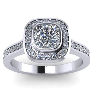 May include: A silver engagement ring with a cushion-cut diamond center stone surrounded by a double halo of smaller diamonds. The band is also set with smaller diamonds.