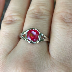 Puede incluir: Un anillo de plata con una piedra preciosa roja engastada en una banda delicada y retorcida.