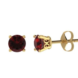 May include: A pair of gold stud earrings with a red gemstone in the center of each earring.