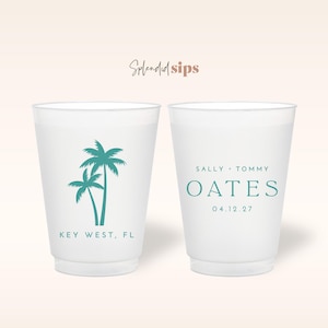 May include: Two white plastic cups with teal palm tree graphics and text. One cup reads "Key West, FL." The other cup has the names "Sally + Tommy Oates" and the date "04.12.27."