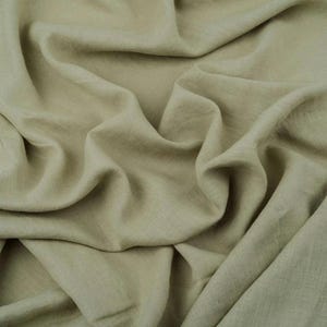 Op de afbeelding: Close-up van een vloeiende, saliegroene stof met zachte plooien en een getextureerd uiterlijk. Het materiaal lijkt lichtgewicht, mogelijk linnen of een vergelijkbare natuurlijke vezel, ideaal voor kleding of woondecoratie.