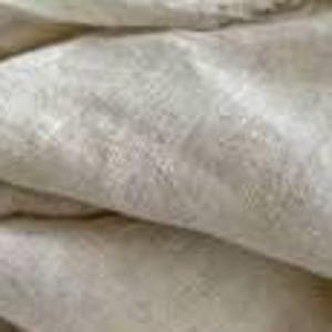 Op de afbeelding: Close-up van gevouwen, gebroken witte linnen stof. De stof heeft een licht getextureerde uitstraling met zichtbare vezels en subtiele kleurvariaties. De plooien cre&euml;ren schaduwen en diepte, wat de natuurlijke textuur van het materiaal benadrukt. De algehele uitstraling is zacht en neutraal.