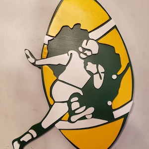 Puede incluir: Silueta de fútbol en forma de balón de fútbol verde y amarillo con una figura blanca corriendo con el balón. La figura lleva un casco y una camiseta.