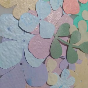 May include: Assortment of pastel colored paper flowers and leaves. The flowers are cut from textured paper and have a glittery finish.
