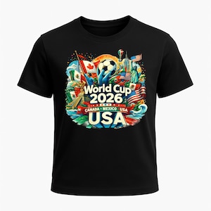 Puede incluir: Camiseta negra con un gr&aacute;fico colorido para la Copa Mundial de 2026, organizada por Canad&aacute;, M&eacute;xico y EE. UU. El dise&ntilde;o incluye un bal&oacute;n de f&uacute;tbol, banderas y monumentos de los tres pa&iacute;ses anfitriones. El texto "World Cup 2026" y "USA" se muestran de forma destacada.