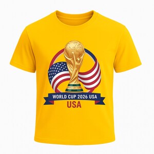 May include: A yellow t-shirt featuring a gold World Cup trophy graphic. The design includes the American flag and the text "WORLD CUP 2026 USA" on a blue banner. The shirt is a short-sleeved crew neck.