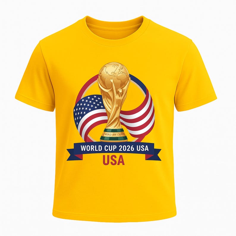 May include: A yellow t-shirt featuring a gold World Cup trophy graphic. The design includes the American flag and the text "WORLD CUP 2026 USA" on a blue banner. The shirt is a short-sleeved crew neck.