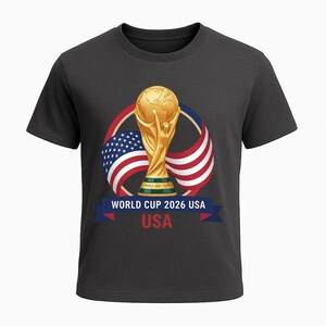 May include: Dark gray t-shirt featuring a gold World Cup trophy graphic. The design includes the American flag and the text "WORLD CUP 2026 USA". The shirt is a crew neck style.