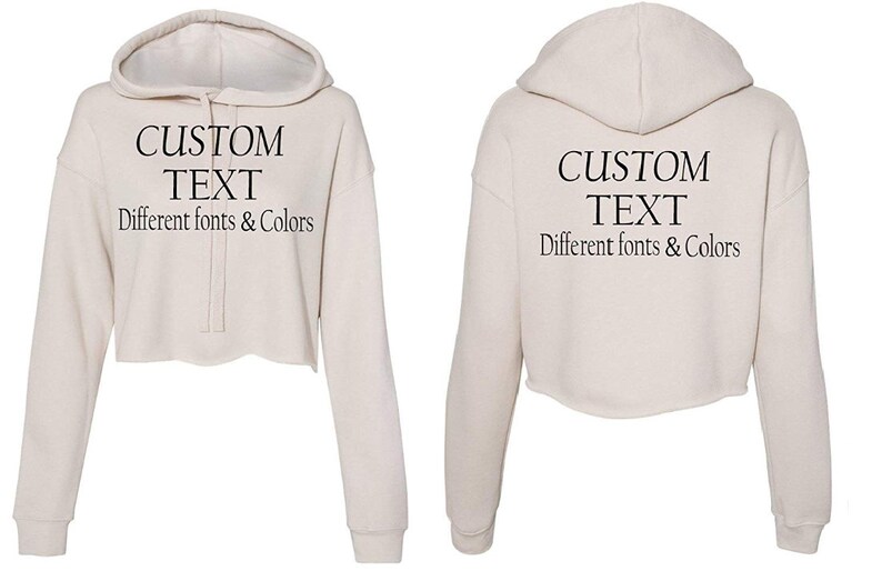 May include: A cream-colored cropped hoodie with a drawstring hood. The hoodie has long sleeves and the text "CUSTOM TEXT Different fonts & Colors" is printed on the front and back.
