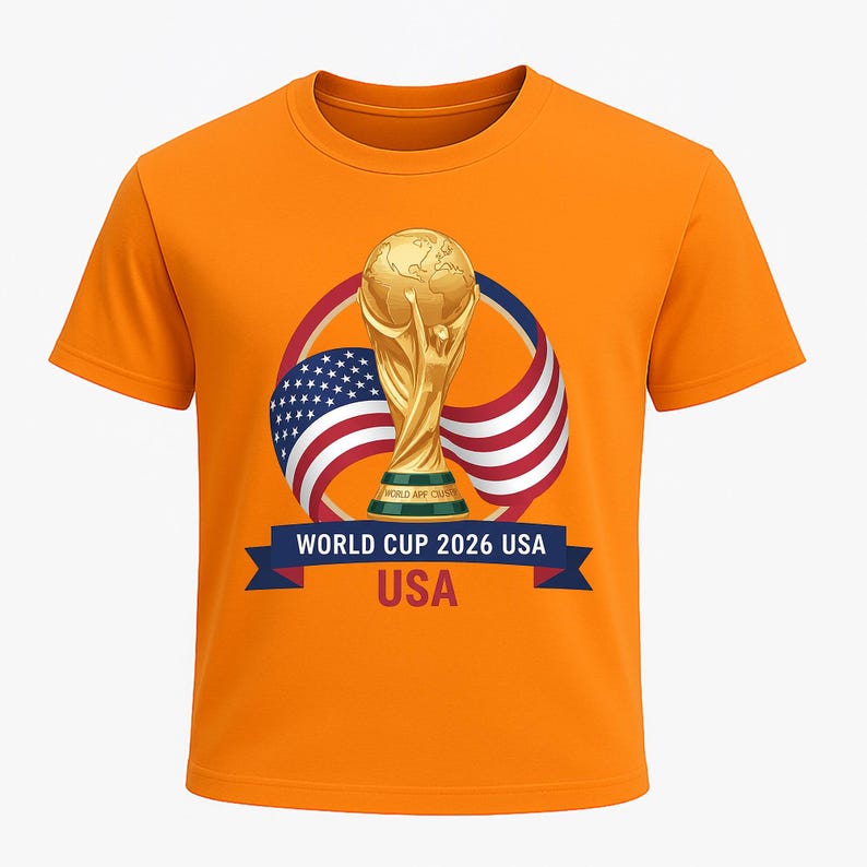 May include: Orange t-shirt featuring a gold trophy, the American flag, and the text "WORLD CUP 2026 USA." The design includes a blue banner with white text. The shirt is a short-sleeved crew neck.
