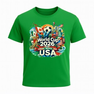 Puede incluir: Camiseta verde con un gr&aacute;fico colorido para la Copa del Mundo 2026. El dise&ntilde;o incluye un bal&oacute;n de f&uacute;tbol, banderas de Canad&aacute;, M&eacute;xico y EE. UU., y la Estatua de la Libertad. El texto "World Cup 2026" y "USA" se muestran.
