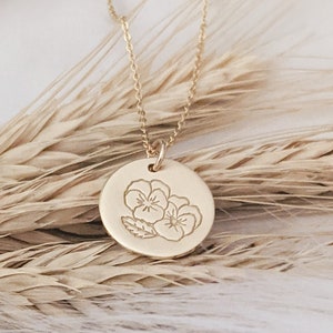 May include: A gold necklace with a round pendant featuring an engraved design of three delicate flowers.