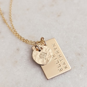 May include: Gold necklace with a rectangular charm engraved with the names "Ellie Kathryn" and a small round charm with a leaf design.