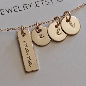 May include: Gold necklace with a bar charm that says "mama" and three round charms with the letters "e", "l", and "b".