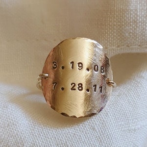May include: Gold ring with a round, textured surface engraved with the dates "3.19.08" and "7.28.11".